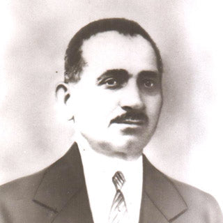 A black and white vintage portrait photograph of a man with a mustache, wearing a suit and tie, shown from the chest up against a soft light background.